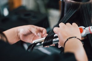 Woman with long dark hair having her hair curled with straighteners